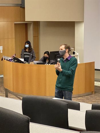 Professor Wade Fagen-Ulmschneider speaks at 2021 ChicTech event, at the front of a classroom with a microphone and wearing a green sweater.