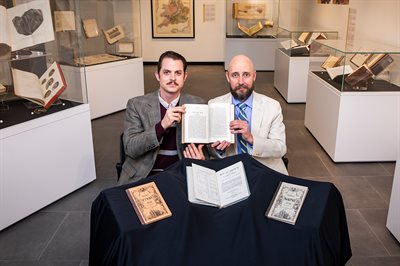Illinois CS professor Neal Davis, left, sits at a desk with Linguistics professor Ryan Shosted, as both hold up a copy hold a copy of the Book of Mormon written in the Deseret Alphabet at the Rare Book and Manuscript Library.