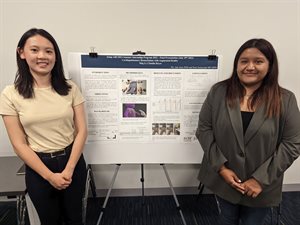 Meg Li (left) and Claudia Reyes stand in front of their research poster.