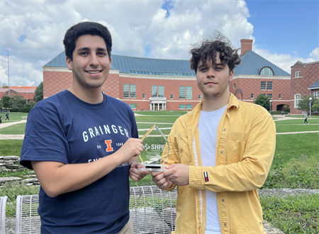 Illinois CS students Federico Cifuentes-Urtubey (left) and Samuil Donchev (right) pose outside near the Grainger College of Engineering Library holding an award.