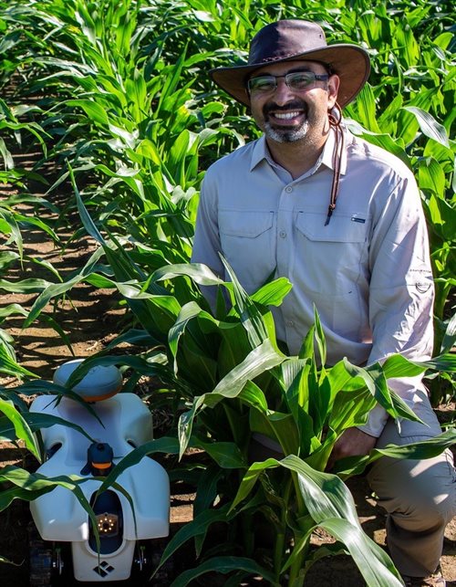 Girish Chowdhary pictured here in a corn field with one of the robots that his company, EarthSense, has created.