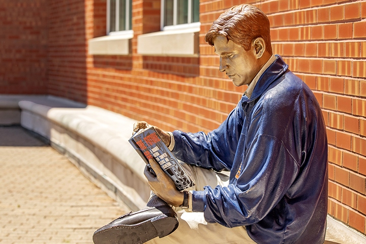 The metal Grainger Bob statue sits and reads a book.