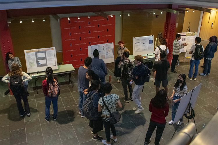 Students stand in a hallway at the Thomas M. Siebel Center for Computer Science, looking at and hearing research project presentations, during the 2022 Trick or Research Event.