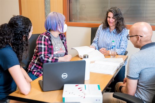 A woman sits at the head of the table teaching three students inside a classroom at the Siebel Center for Computer Science.