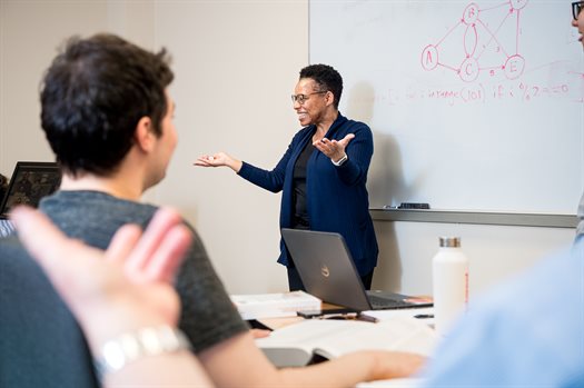 A woman is pointing while teaching students at a whiteboard inside a classroom at the Siebel Center for Computer Science.